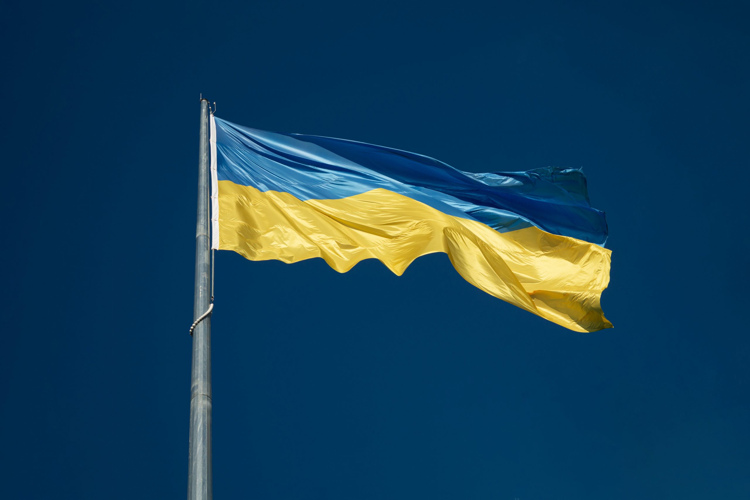 Ukraine flag blowing in wind against a deep blue clear sky backdrop. Image by Yehor Milohrodskyi.