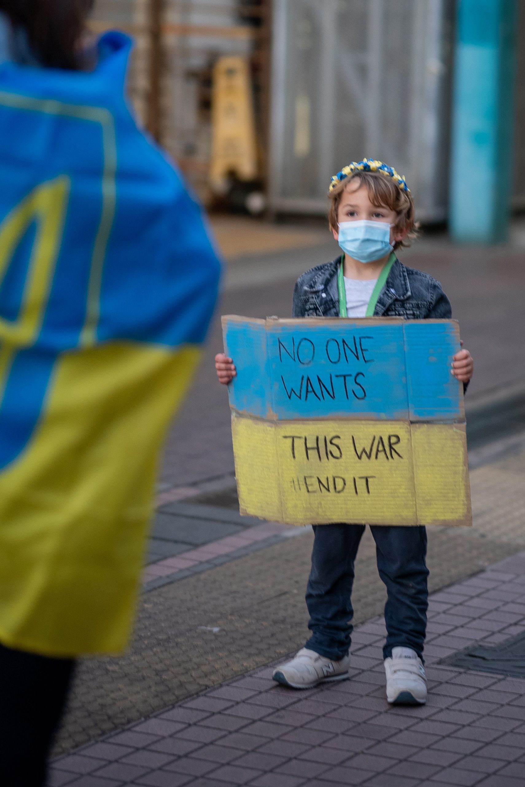 Small boy holding a sign that says NO ONE WANTS THIS WAR END IT.